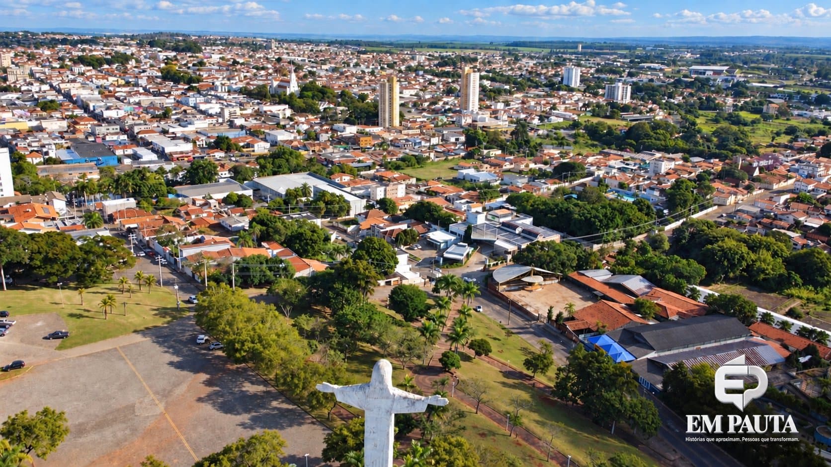 Vista aérea de Avaré mostra grande parte da área urbana da cidade, com bairros residenciais, prédios, áreas verdes e vias. Em primeiro plano, aparece o monumento do Cristo de braços abertos, voltado para a cidade. Ao fundo, o horizonte reúne a expansão urbana e áreas rurais. No canto inferior direito, está aplicada a marca institucional do Em Pauta.