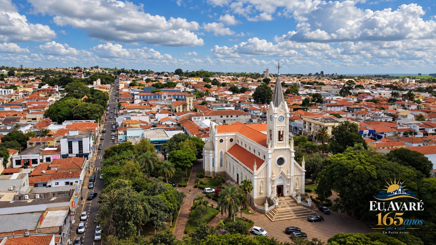 Vista aérea de Avaré mostra a região central da cidade sob céu azul com muitas nuvens. Em destaque, à direita, aparece a Igreja Matriz de Nossa Senhora das Dores, com sua torre alta, telhado avermelhado e área arborizada ao redor. Ao fundo, veem-se ruas, casas, prédios e grande parte da área urbana. No canto inferior direito está a marca comemorativa “Eu, Avaré - 165 anos - 1861 • 2026 - Em Pauta Avaré”, em azul-marinho e dourado.