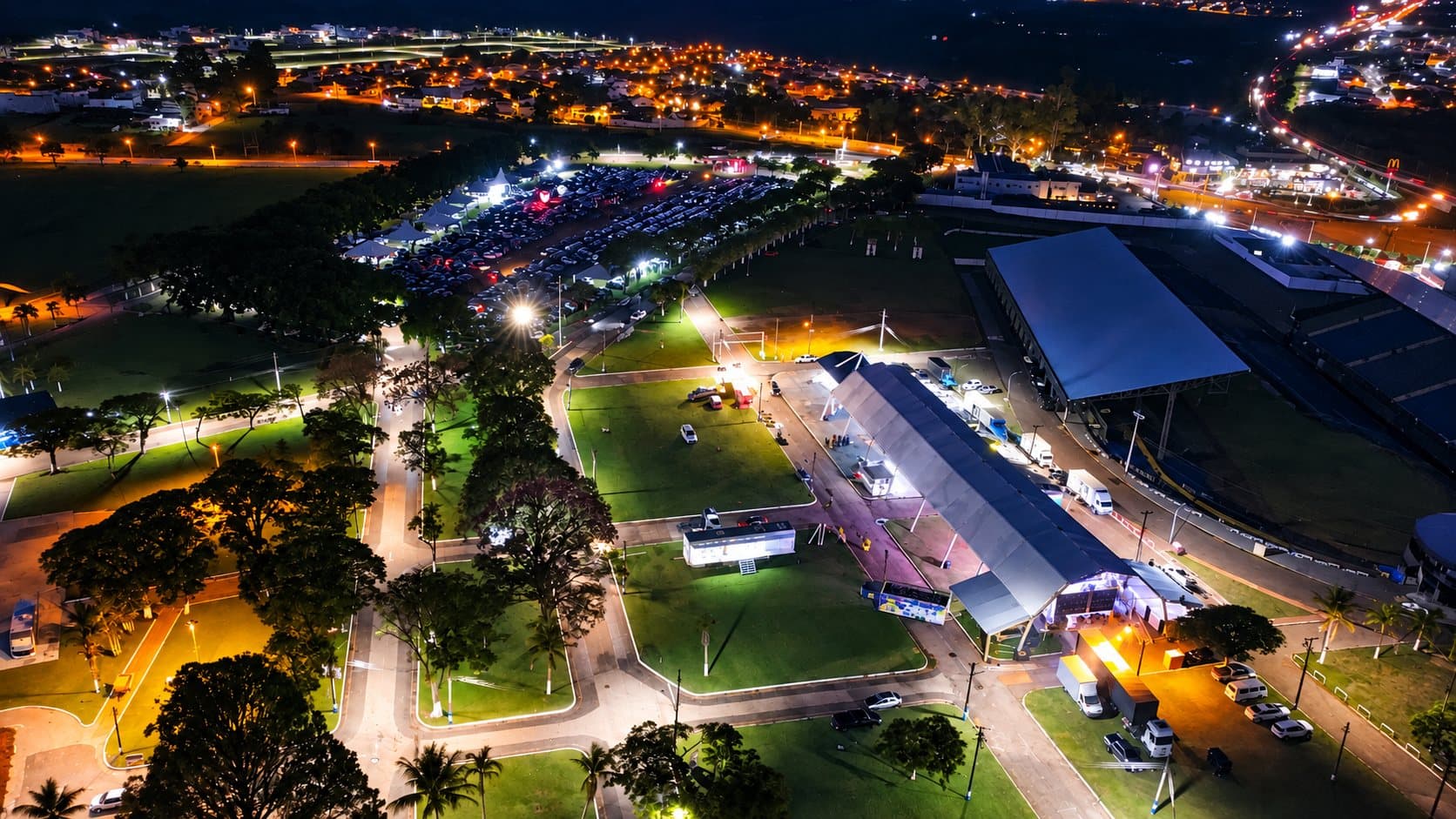 #PraCegoVer: Foto aérea noturna mostra o Parque de Exposições Dr. Fernando Cruz Pimentel, em Avaré, iluminado durante a EMAPA. A imagem registra pavilhões, áreas gramadas, vias internas, estruturas do evento, estacionamento com grande quantidade de veículos e, ao fundo, bairros e avenidas da cidade iluminados.